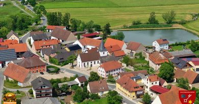 Sanierung der Kirche in Elsendorf beendet. Dorfplatz mit Weiher und Wirtshaus. Straße führt durch Elsendorf